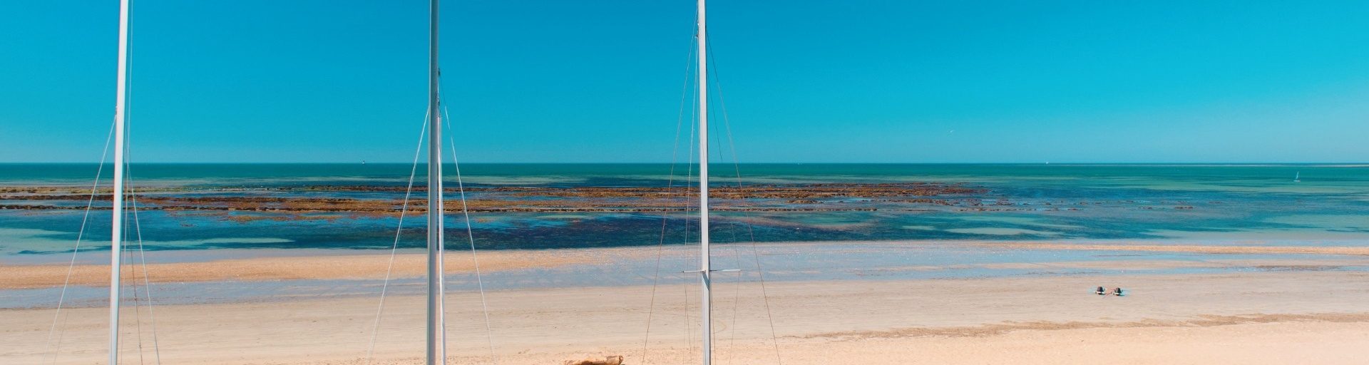 Strand mit türkisfarbenem Meer und Segelbooten.